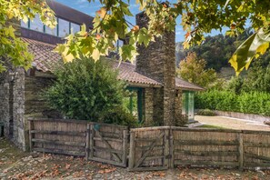 A stone building with a tiled roof, surrounded by a wooden fence and greenery.