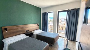 Une chambre d’hôtel avec deux lits simples, une tête de lit en bois, une petite table et un balcon avec des rideaux.