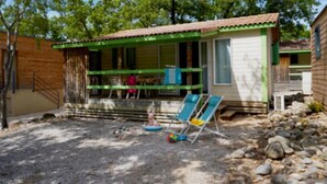 A small, single-story house with a green porch and a covered outdoor seating area.