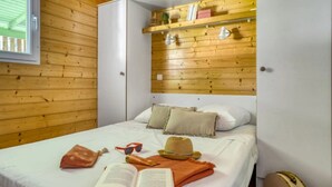 A bedroom with a bed, pillows, a hat, sunglasses, a book, and a suitcase.