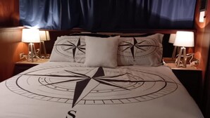 Una cama con diseño de brújula, dos lámparas de noche y una cortina oscura.