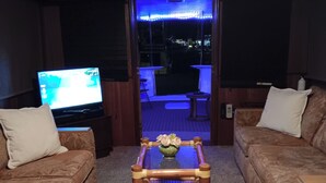 Una sala de estar con dos sofás, una mesa de centro con flores, un televisor y vistas al exterior.