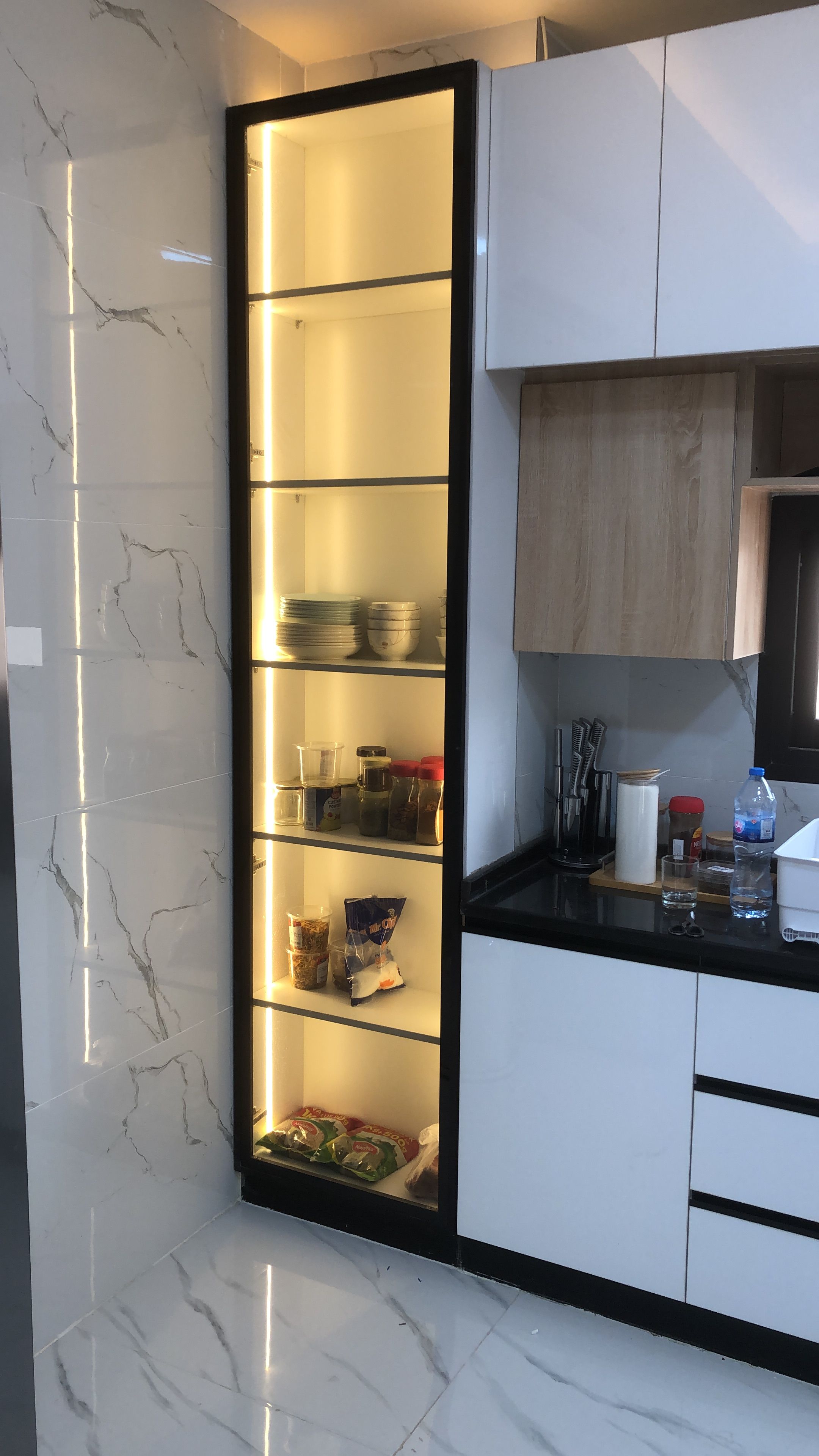 A modern kitchen with a built-in pantry, marble backsplash, and wooden cabinets.