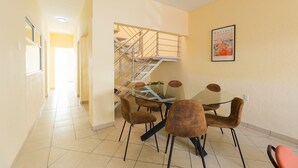 A dining area with a glass table and brown chairs, a staircase, and a framed artwork on the wall. - Casa Chiapas | Stay in the Heart of the City (Puebla)