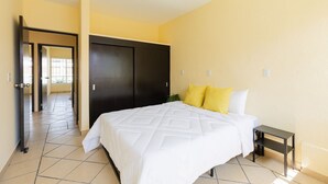 A hotel room with a bed, a nightstand, a wardrobe, and a door leading to another room. - Casa Chiapas | Stay in the Heart of the City (Puebla)