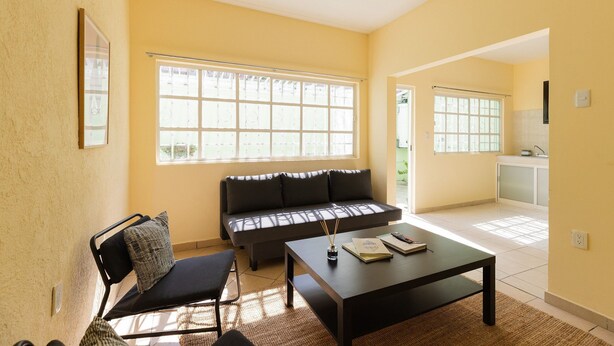A living room with a sofa, a coffee table, and a chair. There are windows providing natural light. - Casa Chiapas | Stay in the Heart of the City (Puebla)