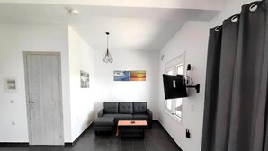 Ein modernes Wohnzimmer mit einer Couch, einem Couchtisch, einem an der Wand befestigten Fernseher und einer Tür.