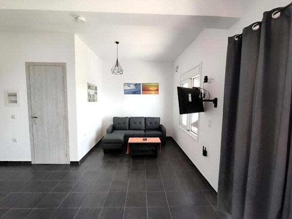 A modern living room with a sofa, a coffee table, a TV mounted on the wall, and a door.