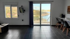 Ein geräumiges Zimmer mit großem Fenster, einem Essbereich und Blick auf eine Küstenlandschaft.