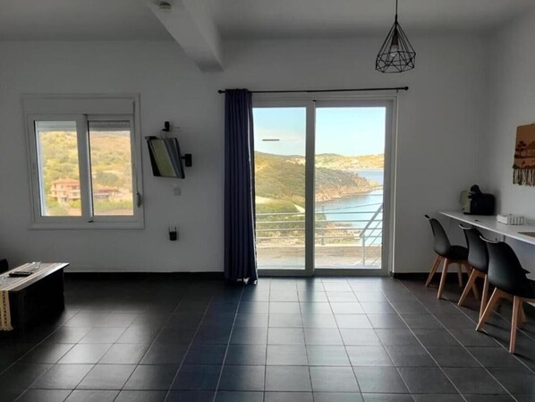 A spacious room with a large window, a dining area, and a view of a coastal landscape.
