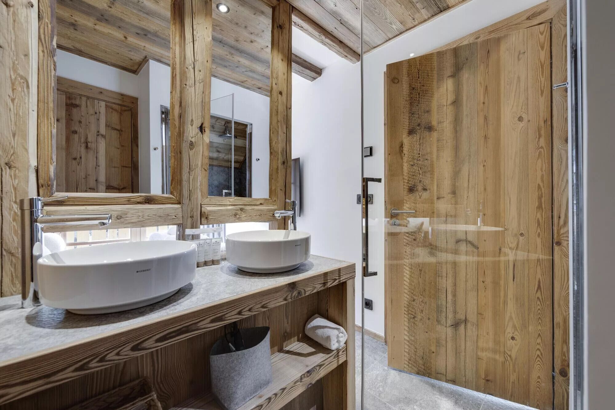 A bathroom with two white sinks, wooden beams on the ceiling, and a glass shower enclosure.