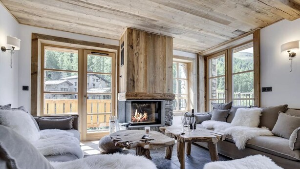 A cozy living room with a fireplace, wooden furniture, and large windows offering a view of the surrounding area. - Stunning High-End Apartment with balcons, Les Rives de l’Isère 3 (Val-d'Isère)