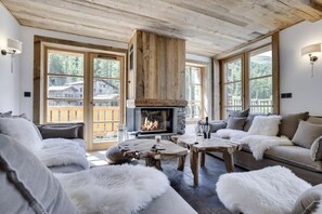 Una sala de estar acogedora con chimenea, muebles de madera y ventanas amplias que ofrecen vistas del entorno.