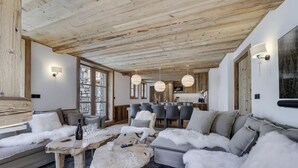 A cozy living room with a wooden ceiling, a stone-framed window, and a dining area with a wooden table and chairs. - Stunning High-End Apartment with balcons, Les Rives de l’Isère 3 (Val-d'Isère)