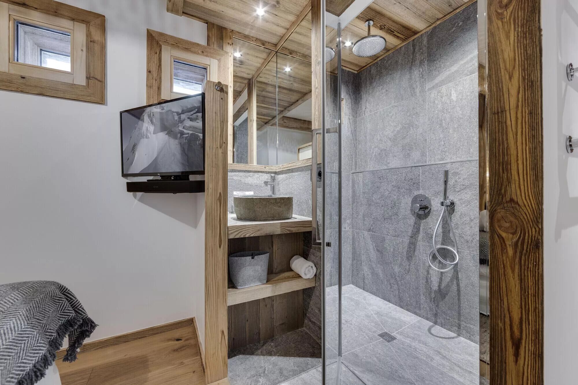 Ein modernes Badezimmer mit Duschkabine aus Glas, Holzboden und einem angebrachten Fernseher.