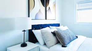 A modern hotel room with a neatly made bed, a bedside lamp, and abstract wall art. - Stylish Mid-Century Modern Home - Near DT Portland for your perfect getaway! (Milwaukie)