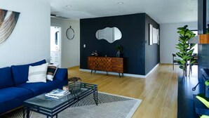 A modern living room with a blue sofa, a glass coffee table, and a wooden cabinet. - Stylish Mid-Century Modern Home - Near DT Portland for your perfect getaway! (Milwaukie)