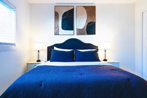 Une chambre à coucher avec un grand lit, deux tables de chevet avec des lampes et des œuvres d’art abstraites accrochées au mur au-dessus du lit.