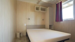 A single bed in a room with wooden walls and a window with curtains. - ZEcamping 4 étoiles familial 2km plage parc aquatique locatif 27m2 (La Faute-sur-Mer)
