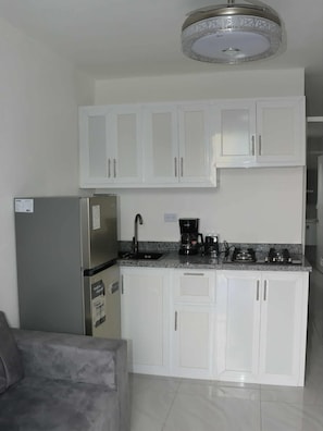 Eine Küche mit weißen Schränken, einem Edelstahl-Kühlschrank, einer Kaffeemaschine und einem Gasherd.