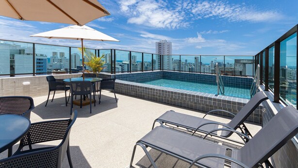 Un espace piscine aménagé sur le toit, avec des chaises longues, une table et des parasols.