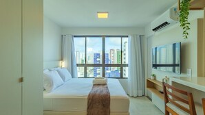 Une chambre d’hôtel équipée d’un lit, d’un bureau, d’une chaise, d’une télévision et offrant une vue sur le paysage urbain.