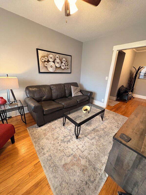 A modern living room with a dark leather sofa, a glass coffee table, and a patterned rug.