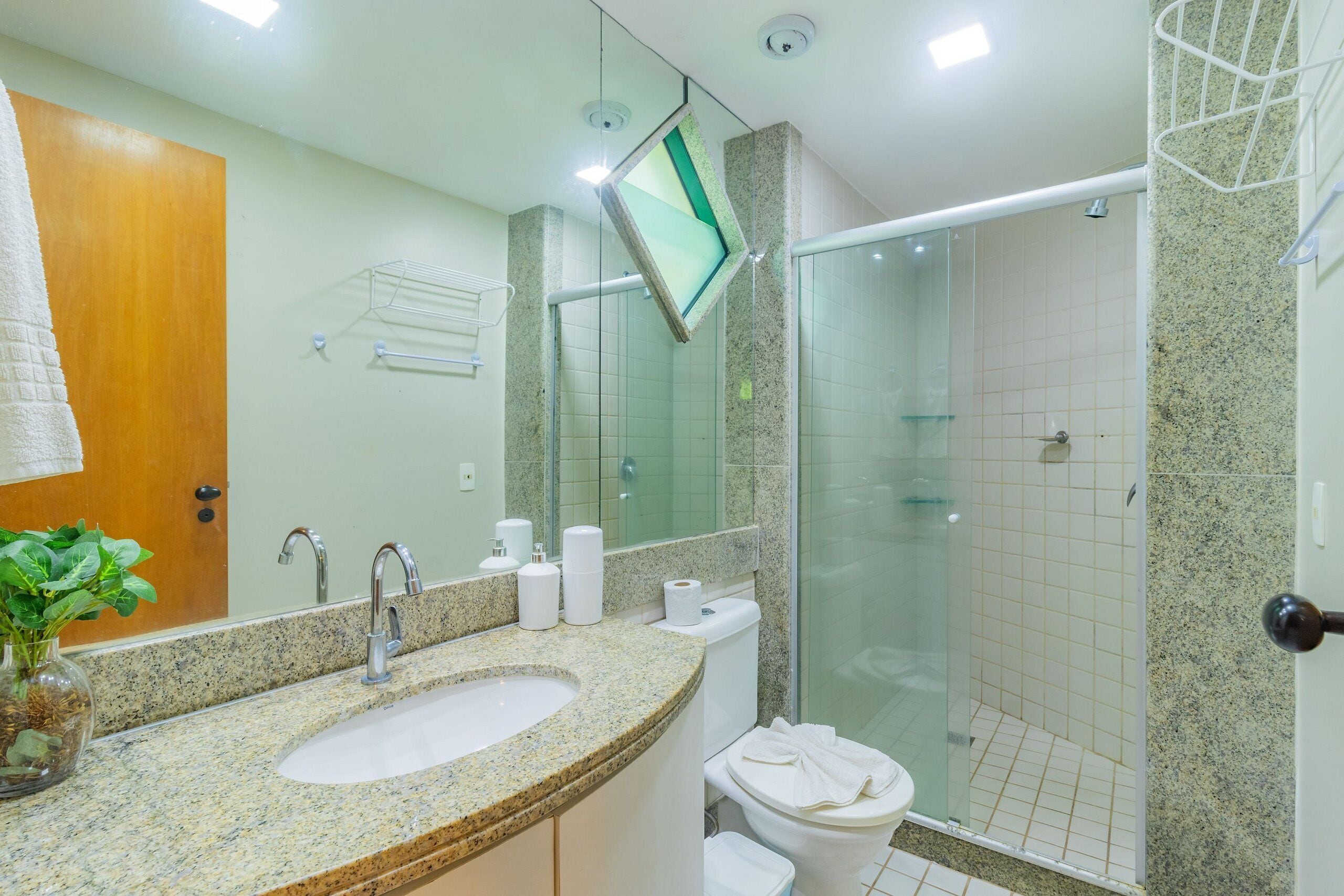 A bathroom with a granite countertop sink, a mirror, a towel rack, and a glass-enclosed shower.
