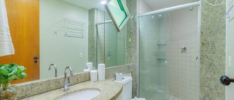 A bathroom with a granite countertop sink, a mirror, a towel rack, and a glass-enclosed shower.