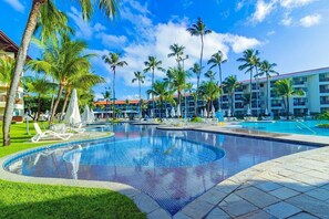 Área de piscina de resort com várias piscinas, palmeiras e espreguiçadeiras.