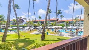 A resort with a swimming pool, palm trees, and a building with a red roof. - Marulhos Suites Resort - Triplo By Carpediem (Ipojuca)