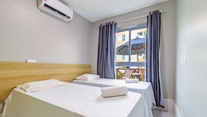 Ein Hotelzimmer mit zwei Betten, einem Holzkopfstück, einem Fenster mit Vorhängen und einer Klimaanlage.