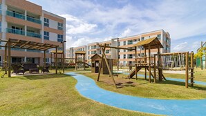 Ein Spielplatz mit blauem Gummibelag, hölzernen Klettergerüsten und einem überdachten Sitzbereich.