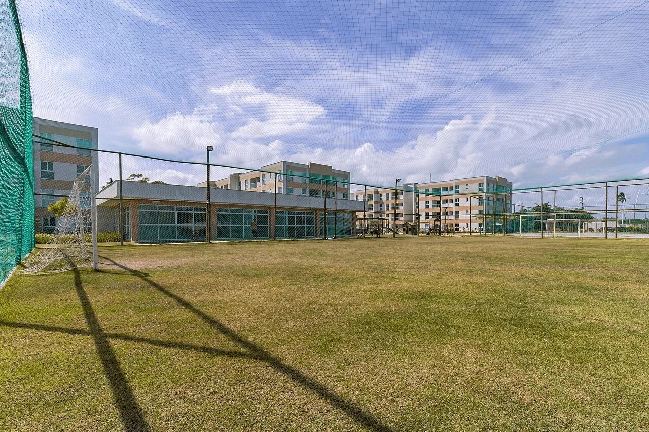 A sports field with a goalpost, surrounded by buildings with large windows and a clear sky.
