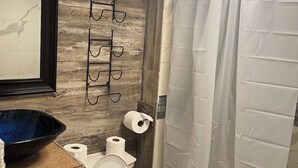 Un baño con tocador de madera, un espejo, inodoro y cortina de ducha.