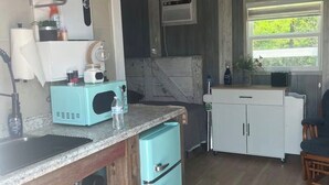 Una cocina compacta con un lavamanos, un microondas, un refrigerador pequeño y una estufa. Hay una ventana con vistas a la vegetación.