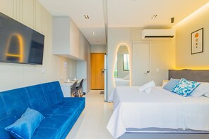 Una habitación de hotel moderna con una cama grande, un sofá azul, un televisor de pantalla plana y un escritorio.