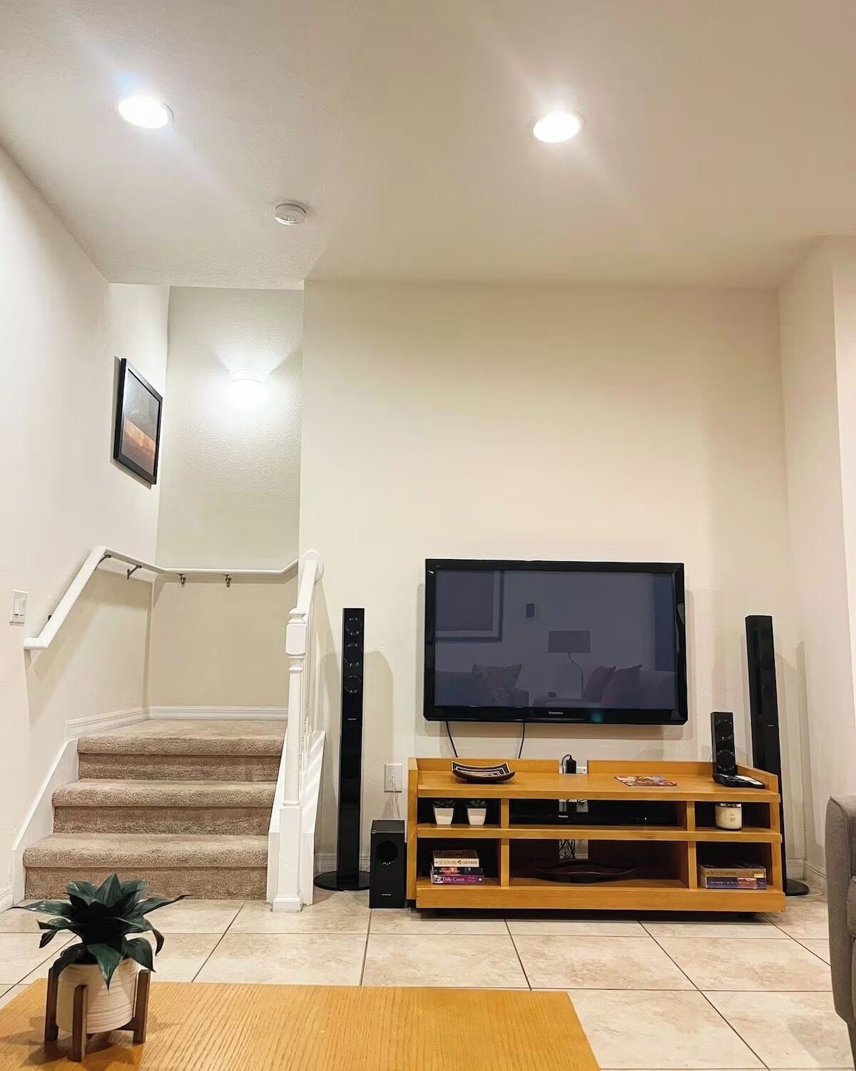 A living room with a staircase, a flat-screen TV, a wooden entertainment unit, and a potted plant.