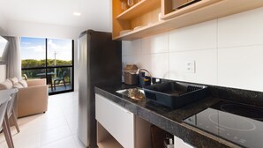 Une cuisine moderne avec un plan de travail noir, un four encastré et une grande fenêtre donnant sur un balcon.