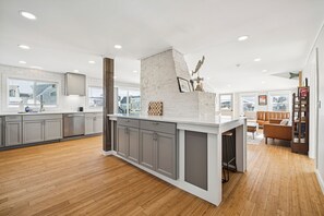 A modern kitchen with grey cabinets, a white island, and wooden flooring. - Riverside Getaway | Newly Renovated | Washer/Dryer (Newbury)