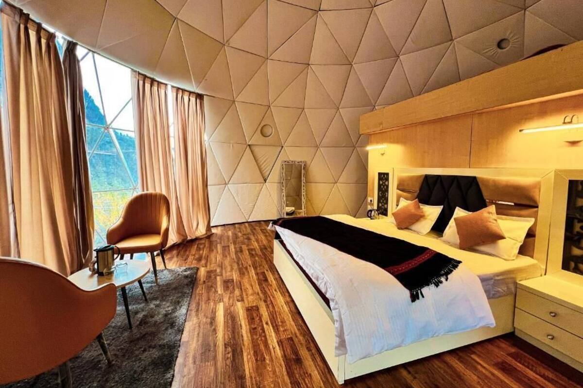 A modern bedroom with a geometric ceiling, a bed with a black and white blanket, a wooden nightstand, and a chair.