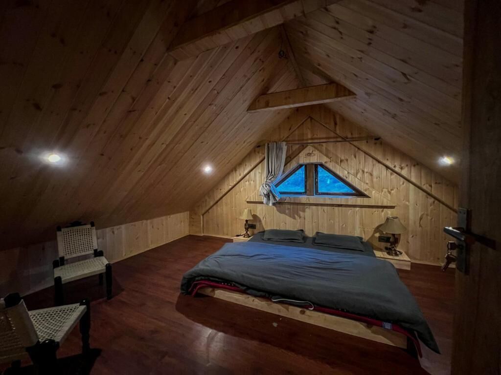 Une chambre mansardée chaleureuse, avec un plafond en pente, un lit, une chaise et une fenêtre.