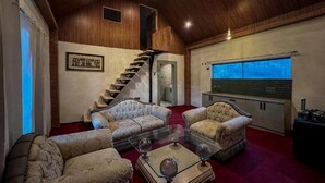 Un salon spacieux avec une moquette rouge, deux canapés confortables, une table basse en verre et un escalier en bois.