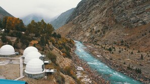A mountainous landscape with a river, white domed structures, and sparse vegetation. - YOLO Outdoors | Riverside Luxury Domes & Glamping — Jispa (Jispa)