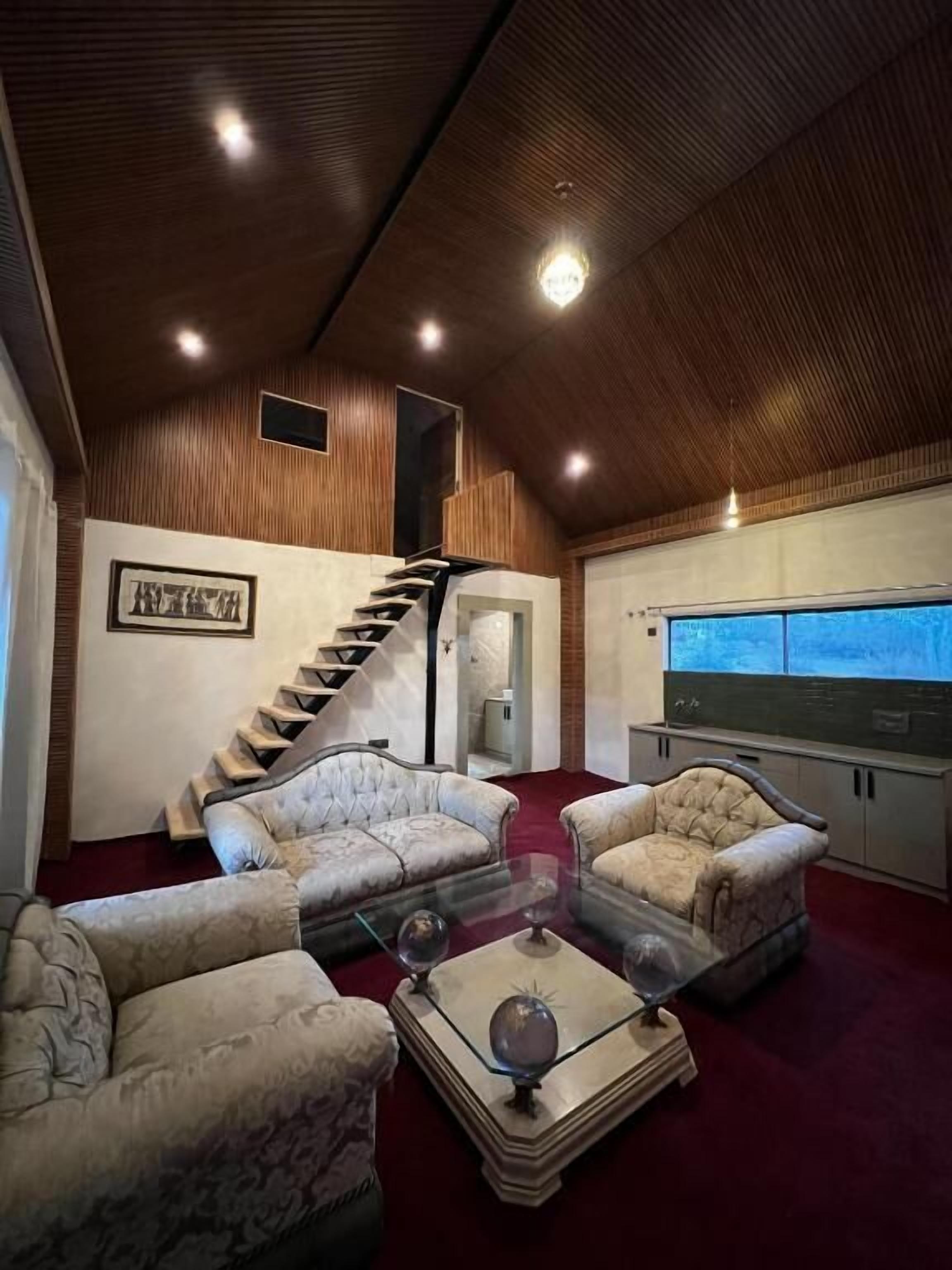A spacious living room with a wooden ceiling, a staircase, and a large window.