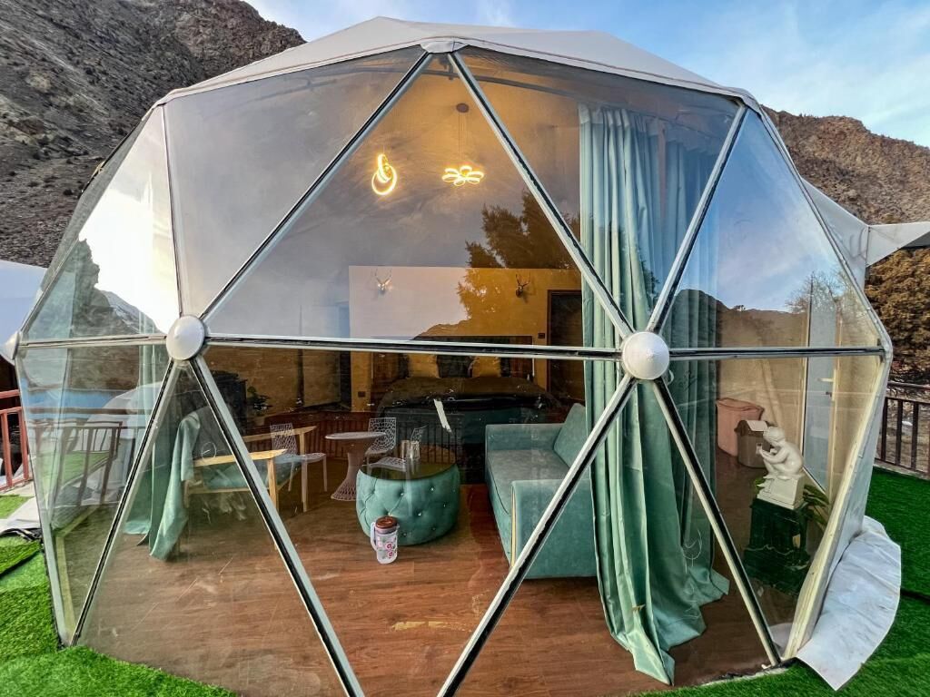 Una estructura de domo geodésico con fachada de vidrio, mobiliario interior y vistas del paisaje circundante.