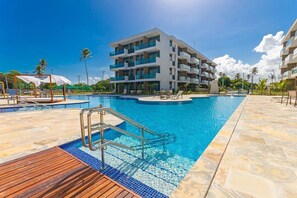 Un hotel moderno con una amplia piscina, varios balcones y una zona de terraza de madera.