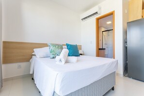 Una cama bien hecha con una colcha blanca, cabecera de madera y almohada color aguamarina.