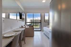 Un hotel moderno con zona de comedor, sofá, cama y ventanas amplias con vistas a la ciudad.