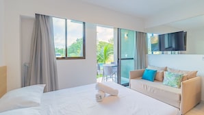 Quarto de hotel moderno com cama, sofá, televisão e varanda com mesa e cadeiras.